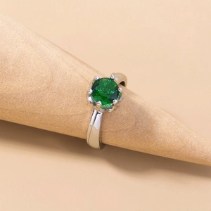 Close-up of classic silver ring with a sparkling round green gemstone on wooden cone