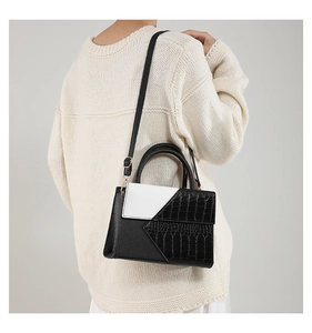 Detailed view of black and white contrast handbag with crocodile texture and shoulder strap