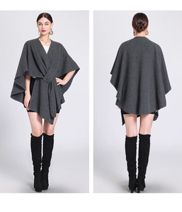 Detail view of dark grey knitted poncho cape with front knot design on studio background