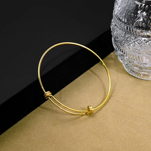 Detail of adjustable gold knot bangle featuring sliding metal loops on a textured surface