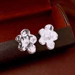 Elegant silver flower earrings with irregular petals and center pearl on leather display