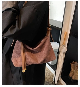Detail of dark brown suede shoulder bag featuring a gold buckle and adjustable strap tail