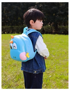 Blue dinosaur hard shell backpack shown on a child during outdoor play in the sunlight
