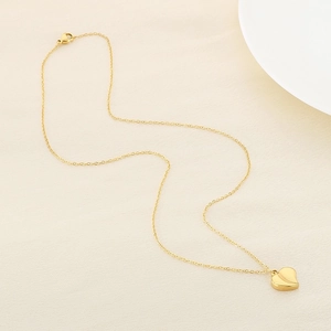 Macro view of gold minimalist heart pendant and fine link chain on soft texture