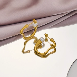 Close-up of irregular gold pearl earrings displayed on elegant purple silk fabric