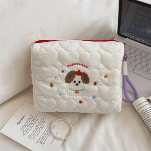 Detail of white quilted puppy makeup bag with embroidery and red zipper on a soft bed