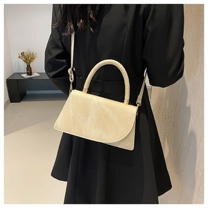 Elegant beige crossbody bag with textured finish and gold buckle shown on a model