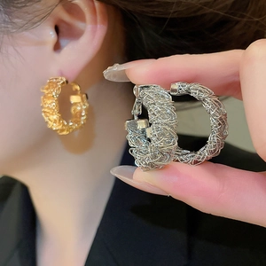 Detail of gold and silver bird nest woven hoop earrings with intricate mesh metal texture