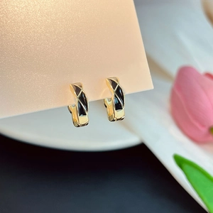 Détail macro de boucles d'oreilles dorées géométriques avec émail noir et motif croisé