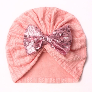 Pink knit baby beanie featuring a large sparkling sequin bow on a soft white background