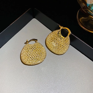 Close-up of golden basket-style woven metal earrings on a dark grey jewelry tray