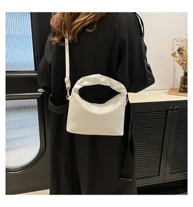 White woven crescent bag with pleated handle shown against a black coat on model