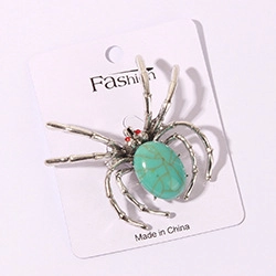 Detailed close-up of a spider brooch featuring a green turquoise stone on a white card