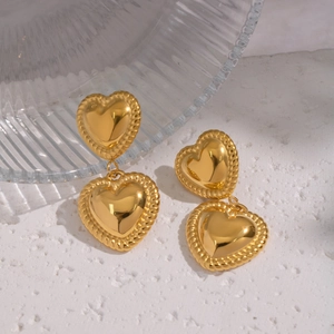 Detailed close-up of double heart gold earrings with vintage rope textured edges on a stone base