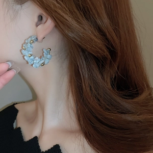 Detail of C-shaped blue beaded hoop earrings with gold accents on model ear