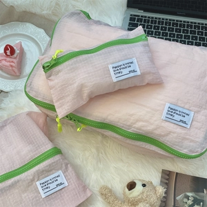 Detail view of pink grid travel organizer bags with vibrant green zippers on plush rug