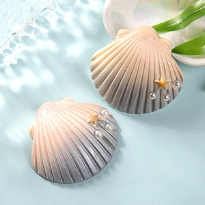 Macro detail of gradient resin shell charms with gold starfish and pearls on blue water background