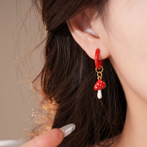 Detail of mushroom pendant earring with red enamel finish and small hoop on a model