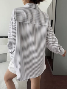 Back view of a white and black striped loose shirt for women in a natural home setting