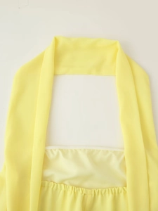Detailed view of yellow halter neckline and pleated fabric on a minimalist A-line dress