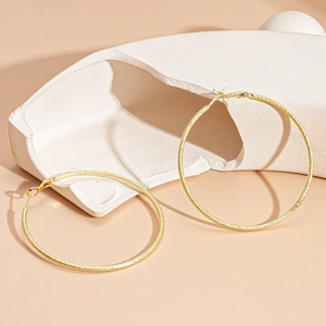Detailed view of large gold hoop earrings with a textured matte finish on stone props