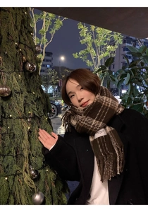 Close-up of a brown plaid scarf with fringe worn by a model in a warm festive setting