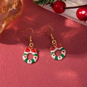Detailed close-up of Christmas wreath earrings with red bows on festive red background