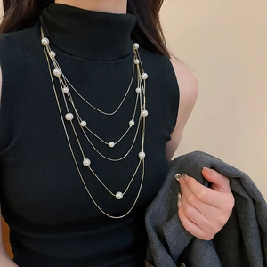 Elegant multi-layered gold chain necklace with white pearls on a black turtleneck