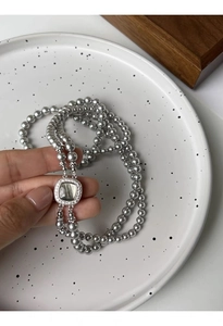 Detailed macro of grey glass pearls with square shell buckle on multi-layer necklace