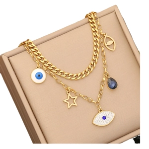 Gold double-layered stainless steel necklace with evil eye and star charms on beige box