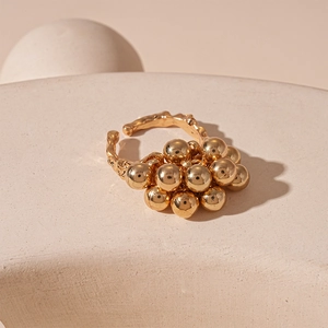 Macro shot of gold sphere cluster ring on white textured stand in warm lighting