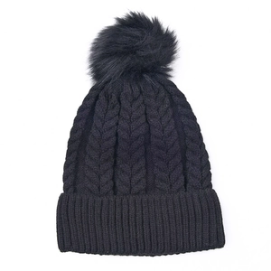 Détail d'un bonnet d'hiver noir en maille torsadée avec un pompon en fausse fourrure