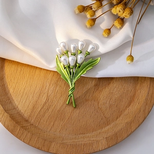 Detail of green enamel leaf brooch with white pearls displayed on a wooden tray