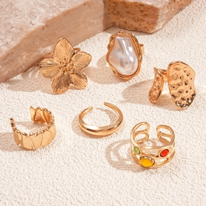 Close-up of golden vintage rings with flower and pearl details on sandy stone surface