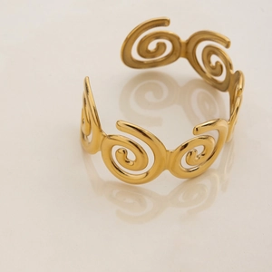 Detail of a spiral C-shaped gold stainless steel bracelet with a high-polished mirror finish