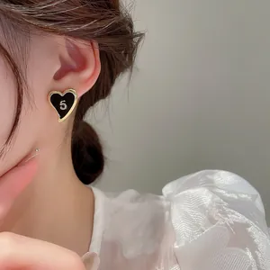 Close-up of heart-shaped black enamel earrings with gold number 5 on a model's ear