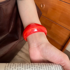 Detailed view of wide translucent red acrylic cuff bracelet on a model's wrist