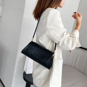 Classic black crocodile pattern shoulder bag with gold hardware worn by a model in a suit