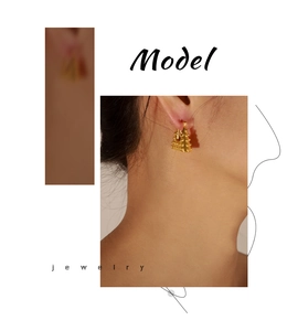 Close-up of geometric gold-plated earrings with metal beads worn by a model