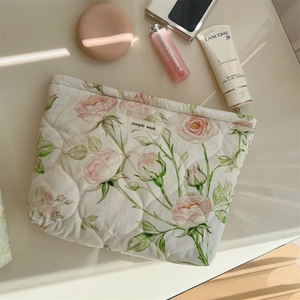 Quilted cotton makeup bag with pink roses and luxury cosmetics in top-view scene