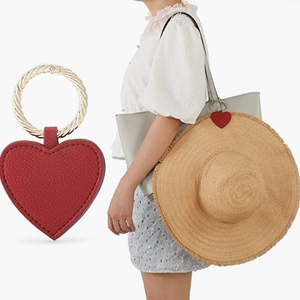 Detail of red heart leather hat clip with golden metal ring attached to a straw hat on a bag