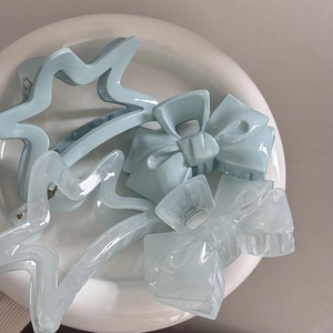 Flat lay of four light blue acrylic hair clips featuring star and bow shapes in a white dish