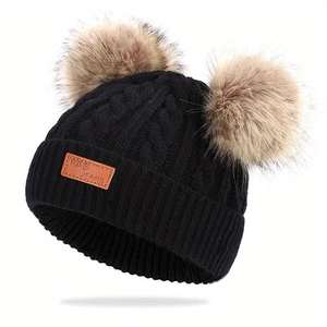 Détail du bonnet en maille torsadée pour bébé avec deux pompons en fausse fourrure