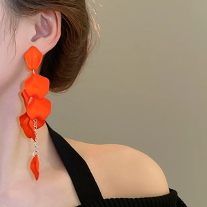 Close-up of model wearing long orange floral petal tassel earrings with gold chains