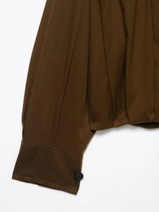 Detailed macro view of dark brown twill fabric sleeve with pleated hem and single black button