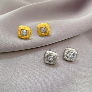 Detail view of square zircon earrings with radial brushed texture on purple silk