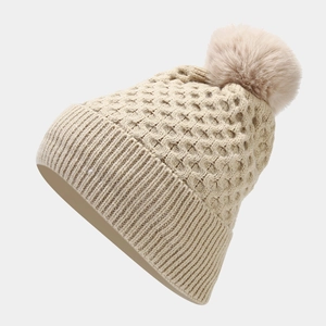 Detail of beige cable-knit beanie with a soft faux fur pom-pom and thick ribbed texture
