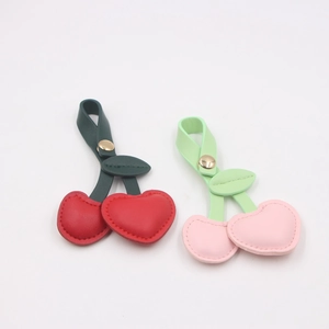 Detail view of red and pink leather cherry keychains with green leaves and gold snaps