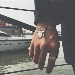 Detail of silver stretch bracelet with 'YOU VS YOU' engraved tag and dumbbell charm