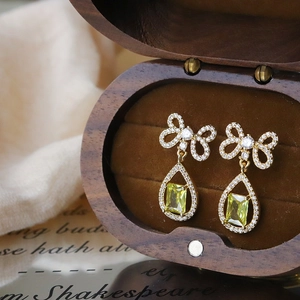 Close-up of golden bow earrings with water drop zircon set in a wooden jewelry box